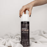 Magic Foam Schaumreiniger-Dose auf weißer Decke mit neutralem Hintergrund. Hand greift von oben rechts nach der Dose.