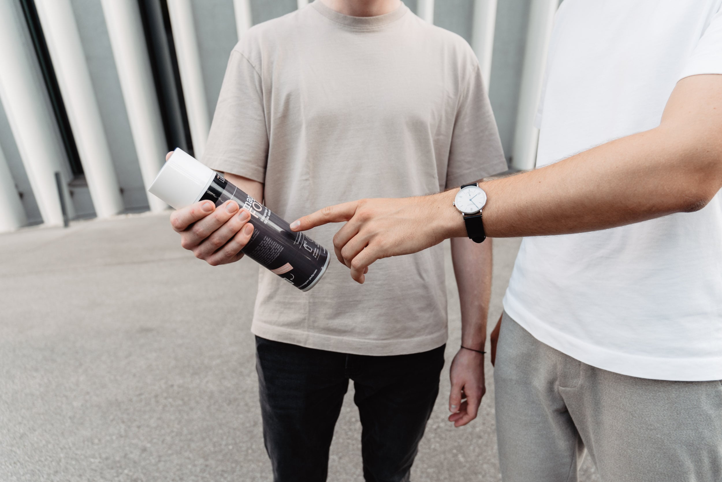 Zwei Personen mit Oberkörperansicht, jeweils in T-Shirts. Eine Person hält eine Magic Foam Dose, während die andere darauf zeigt.