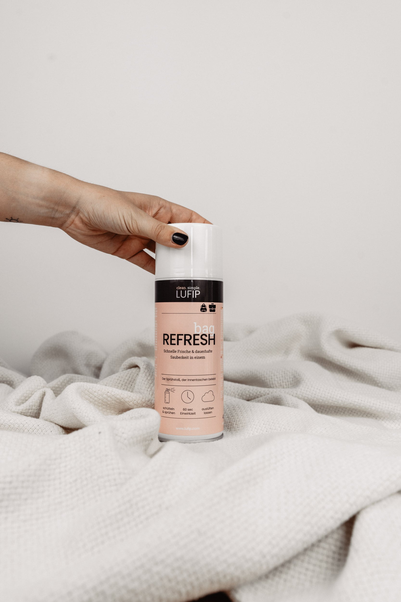 Bag Refresh: Hand greift von links nach dem Produkt auf weißer Decke vor neutralem Hintergrund.