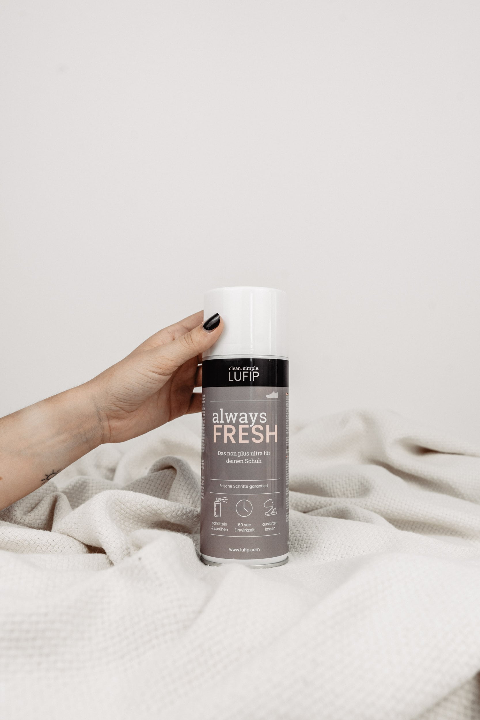 Im Bild ist das Produkt 'Always Fresh' zu sehen, das auf einer weißen Decke vor einem neutralen Hintergrund platziert ist. Eine Hand, von rechts kommend, greift nach dem Produkt. 'Always Fresh' ist ein Produkt zur Geruchsbekämpfung und Bakterienprävention für Schuhe, effektiv und vielseitig für alle Schuharten. Die Szene betont die Hand, die nach diesem Produkt greift, um seine Anwendung oder seine Wirksamkeit zu veranschaulichen.