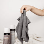 Auf einer weißen Decke vor neutralem Hintergrund ist ein Set zu sehen, wobei das Magic Towel vorn gehalten wird.