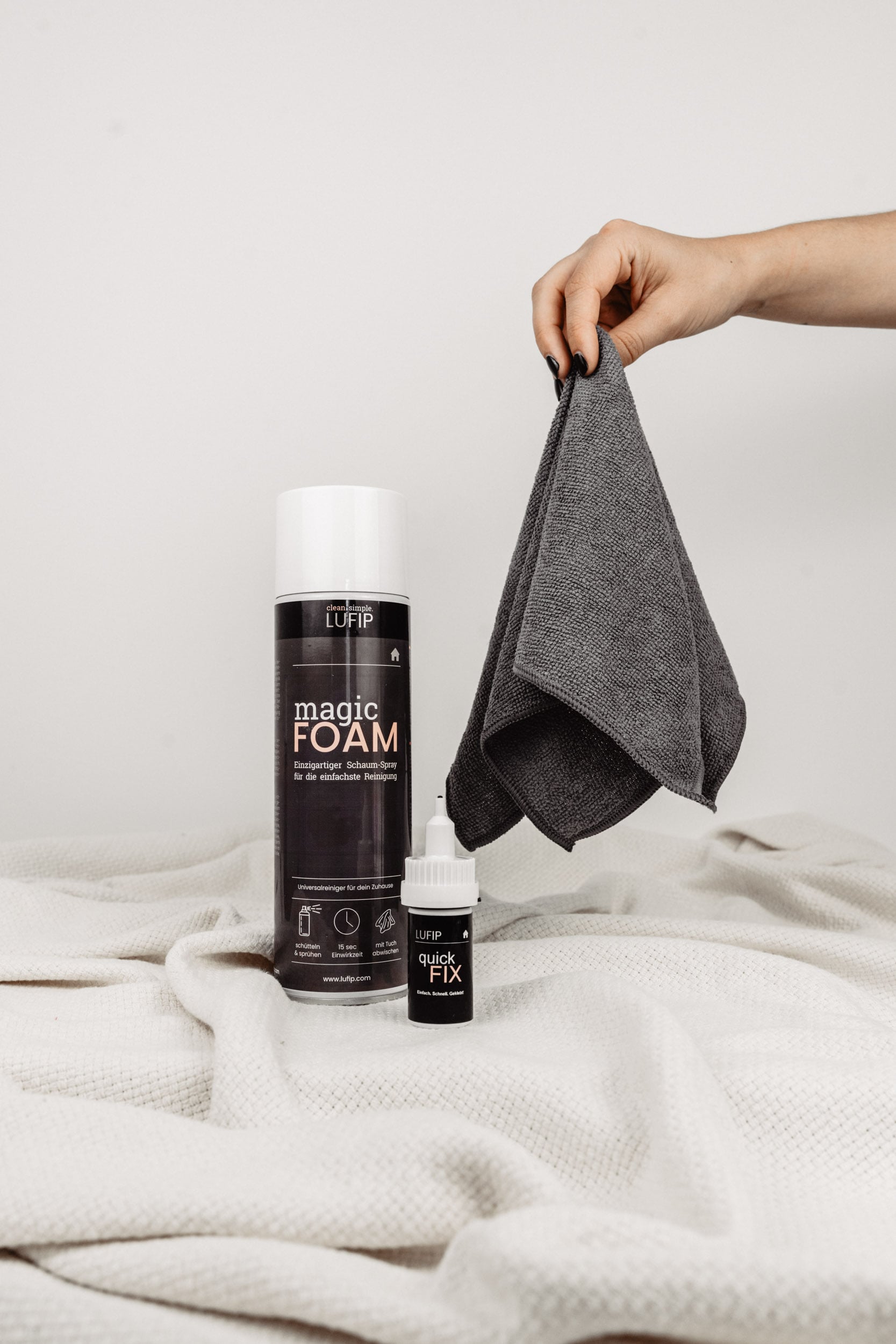 Magic Towel, Magic Foam und Quick Fix vor neutralem Hintergrund mit einer weißen Decke am Boden. Vielseitige Reinigungstücher, Schaumreiniger und Superkleber für verschiedene Reinigungs- und Reparaturaufgaben.