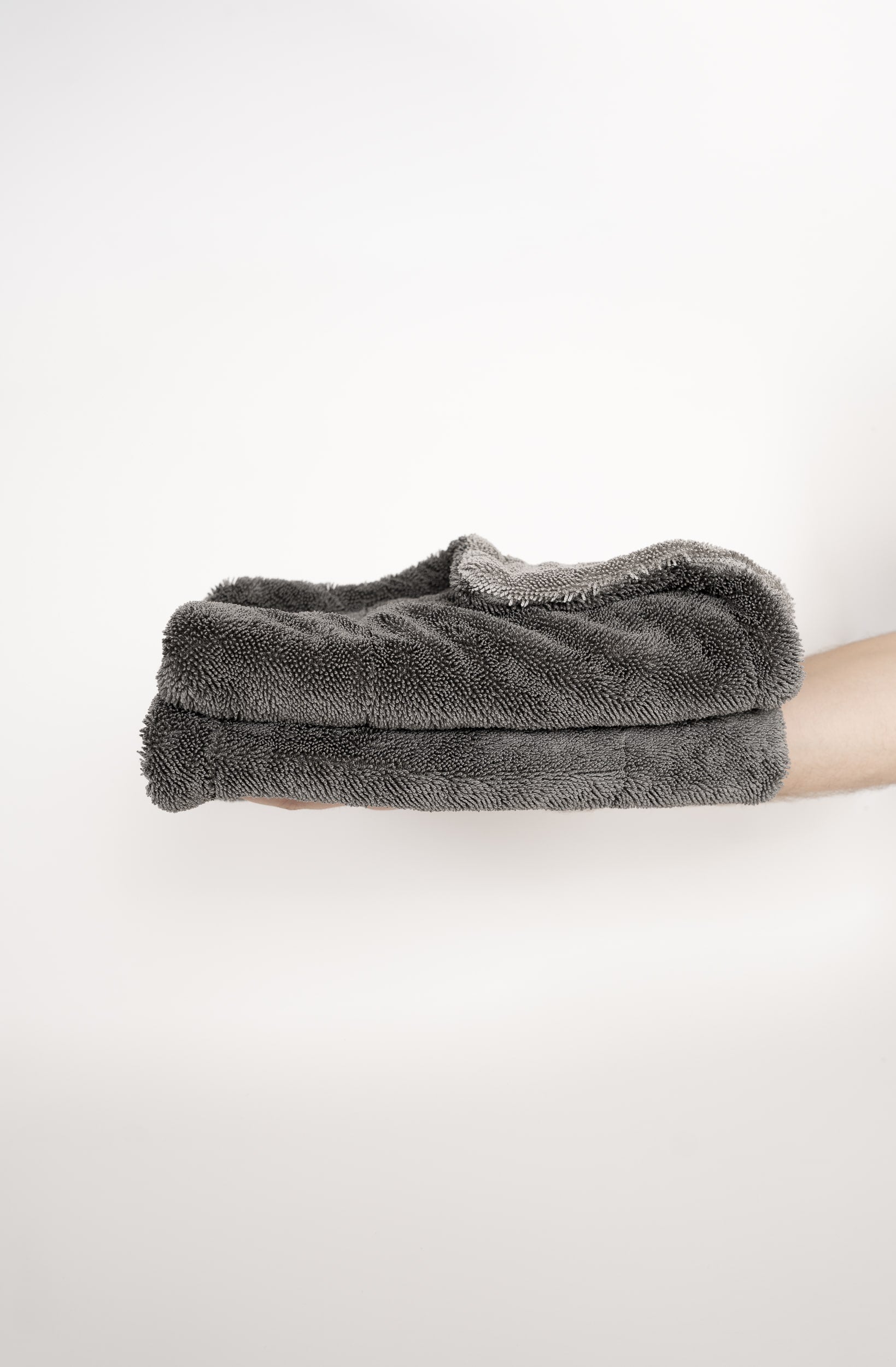 Ein Stapel aus zwei Dry Towels von LUFIP wird auf einer ausgestreckten Hand präsentiert. Der neutrale Hintergrund betont die kompakte Größe und die weiche, saugfähige Textur des Produkts. Perfekt für effizientes und müheloses Trocknen.
