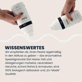 Zwei Hände kippen je eine LUFIP Drain Pearls Flasche über einem hellen Hintergrund; Infotext „Wissenswertes“ erklärt regelmäßige Anwendung, enzymaktive Formel, Geruchsneutralisation und 100 % biologische Abbaubarkeit.
